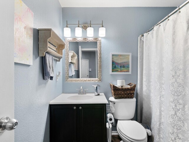 full bath featuring vanity, toilet, and a textured wall