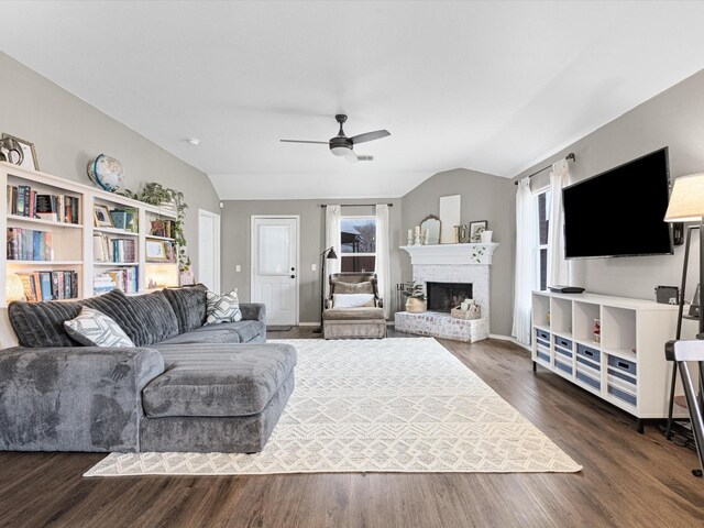 living room featuring vaulted ceiling, ceiling fan, dark wood-style flooring, a fireplace, and baseboards