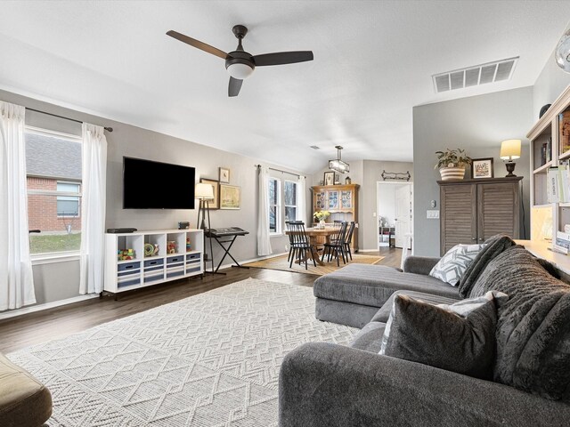 living area with vaulted ceiling, a ceiling fan, wood finished floors, baseboards, and visible vents