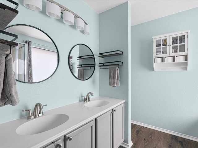 full bath with double vanity, wood finished floors, baseboards, and a sink