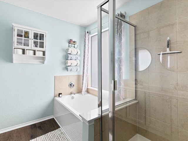 full bath featuring wood finished floors, a bath, a stall shower, and baseboards