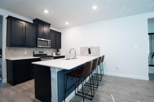 kitchen featuring tasteful backsplash, sink, light hardwood / wood-style flooring, appliances with stainless steel finishes, and a kitchen breakfast bar