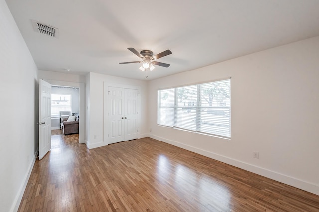 unfurnished bedroom with ceiling fan, a closet, multiple windows, and light hardwood / wood-style floors