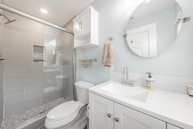 bathroom featuring toilet, vanity, and a shower with door