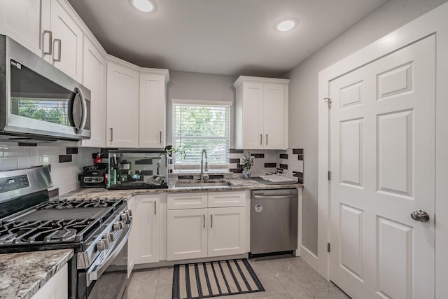 kitchen with appliances with stainless steel finishes, white cabinetry, light stone counters, and sink