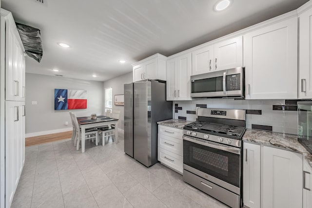 kitchen with appliances with stainless steel finishes, white cabinetry, tasteful backsplash, light stone counters, and light tile patterned floors