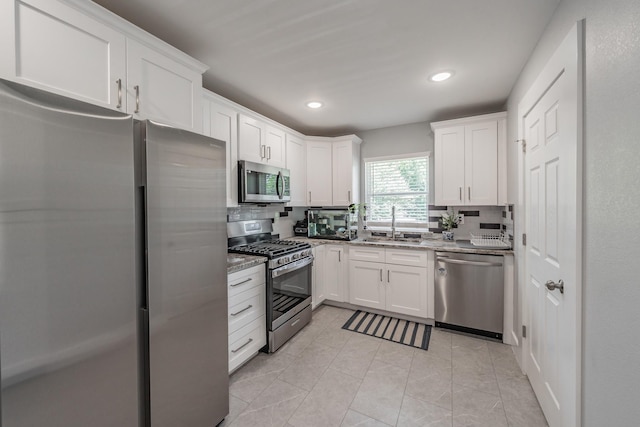 kitchen with appliances with stainless steel finishes, decorative backsplash, white cabinets, and light stone counters