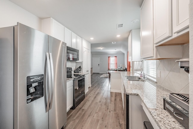 kitchen with light hardwood / wood-style floors, black appliances, white cabinets, light stone counters, and sink