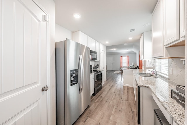 kitchen featuring white cabinetry, stainless steel appliances, light wood-type flooring, light stone counters, and sink