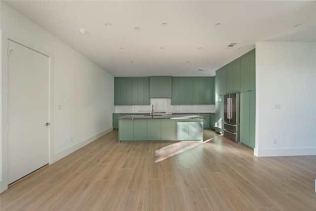 kitchen with a kitchen island with sink, green cabinets, high quality fridge, and light hardwood / wood-style flooring