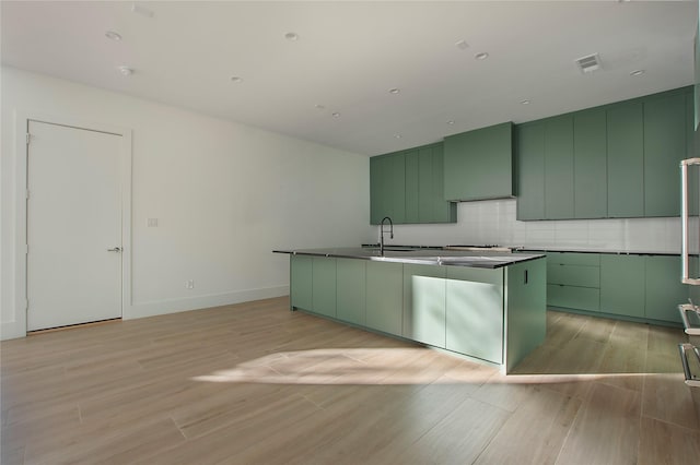 kitchen with backsplash, green cabinets, wall chimney exhaust hood, and an island with sink