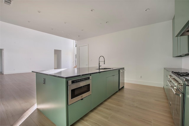 kitchen featuring an island with sink, green cabinets, stainless steel appliances, light hardwood / wood-style flooring, and sink