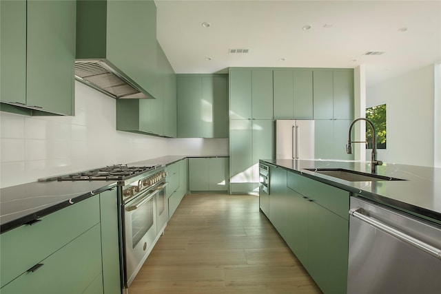 kitchen with sink, wall chimney range hood, green cabinetry, and high quality appliances