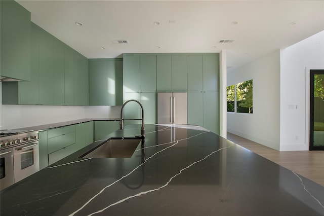 kitchen with sink, hardwood / wood-style floors, green cabinets, and appliances with stainless steel finishes