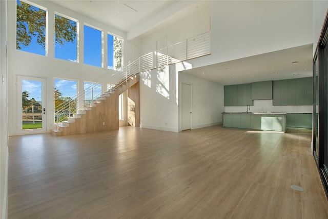 unfurnished living room with sink, a high ceiling, and light hardwood / wood-style flooring