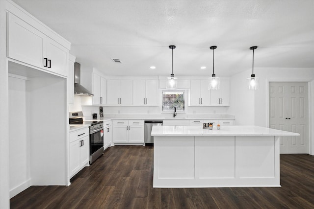 kitchen with stainless steel appliances, pendant lighting, wall chimney exhaust hood, white cabinets, and sink