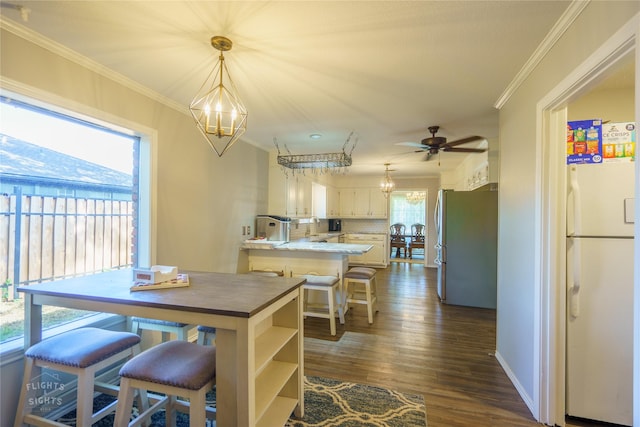 kitchen with white fridge, pendant lighting, kitchen peninsula, ornamental molding, and stainless steel fridge