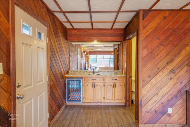 bar with wine cooler, dark hardwood / wood-style floors, wood walls, light stone counters, and coffered ceiling