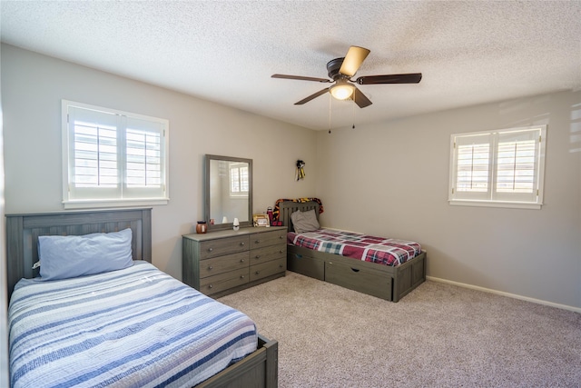 bedroom with ceiling fan, light colored carpet, multiple windows, and a textured ceiling