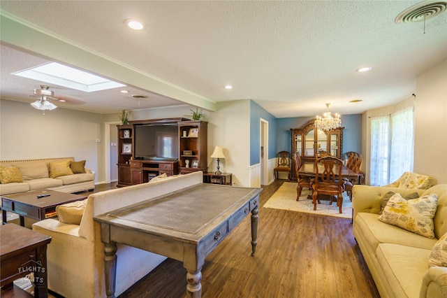 living room with hardwood / wood-style flooring, a textured ceiling, a skylight, and ceiling fan with notable chandelier