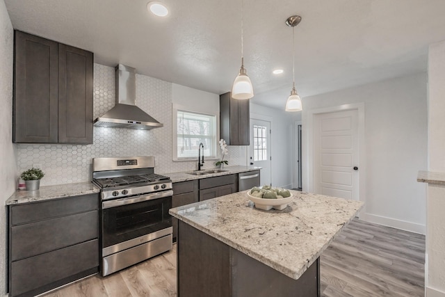 kitchen with dark brown cabinetry, wall chimney range hood, stainless steel appliances, sink, and hanging light fixtures