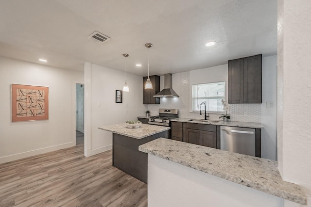 kitchen featuring wall chimney range hood, stainless steel appliances, decorative backsplash, sink, and hanging light fixtures