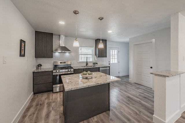 kitchen with a kitchen island, decorative light fixtures, wall chimney range hood, stainless steel appliances, and sink