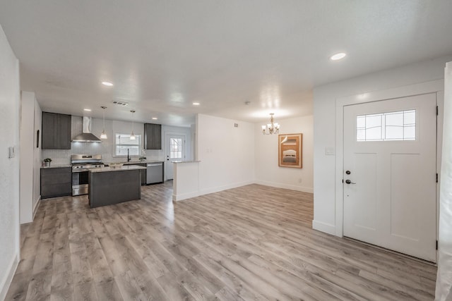 kitchen featuring decorative light fixtures, decorative backsplash, light hardwood / wood-style flooring, appliances with stainless steel finishes, and wall chimney exhaust hood