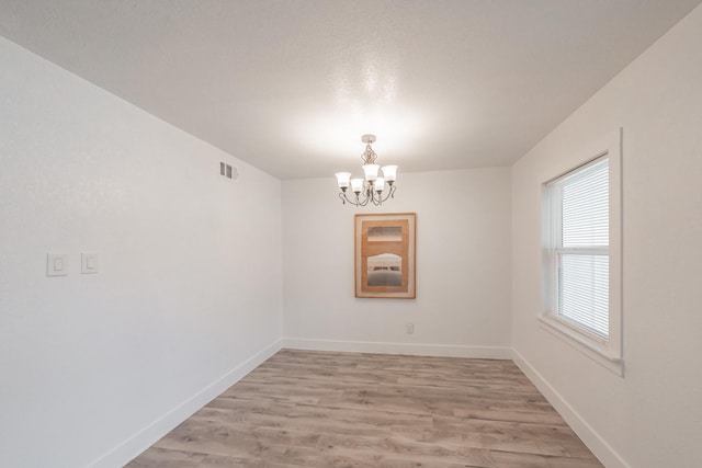 spare room featuring light wood-type flooring and a notable chandelier