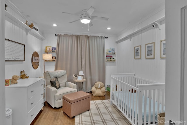 bedroom featuring ceiling fan, a nursery area, ornamental molding, and light wood-type flooring