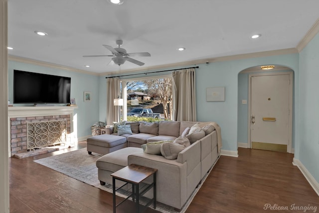 living room with ceiling fan, a fireplace, dark hardwood / wood-style flooring, and crown molding