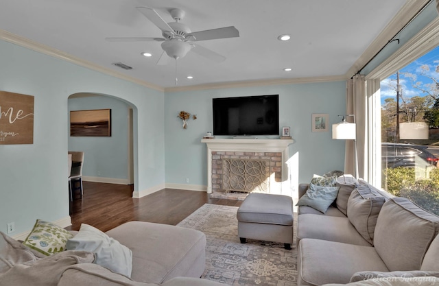 living room with a brick fireplace, dark hardwood / wood-style flooring, crown molding, and ceiling fan