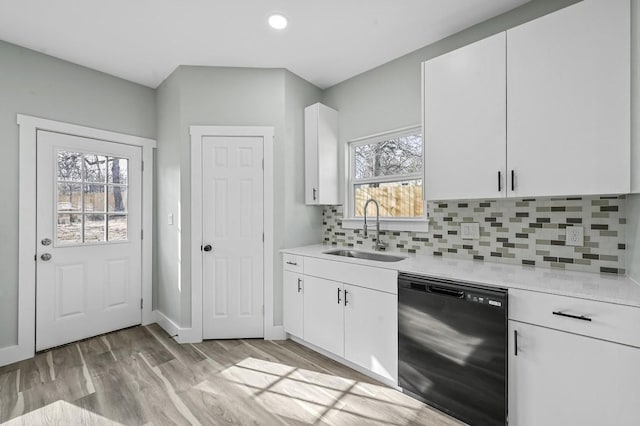 kitchen featuring backsplash, sink, black dishwasher, white cabinetry, and light wood-type flooring