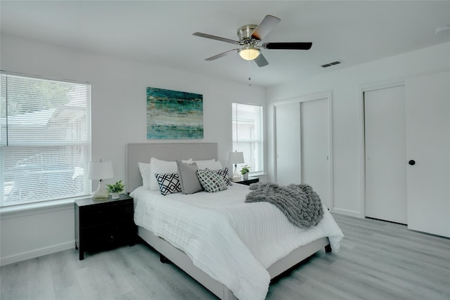 bedroom featuring ceiling fan, multiple closets, and light hardwood / wood-style flooring