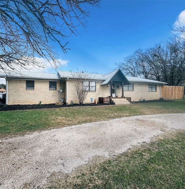 ranch-style home with metal roof, brick siding, a front yard, and fence