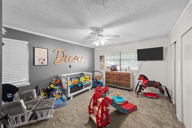 carpeted bedroom with ceiling fan, a textured ceiling, ornamental molding, and a crib