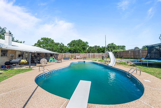 view of pool with a patio area, a water slide, a diving board, and a trampoline