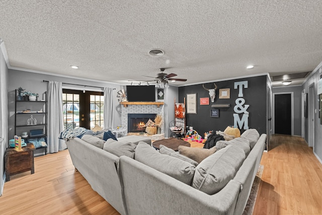 living area with a fireplace, wood finished floors, visible vents, and crown molding