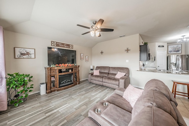 living room featuring ceiling fan, lofted ceiling, and light wood-type flooring