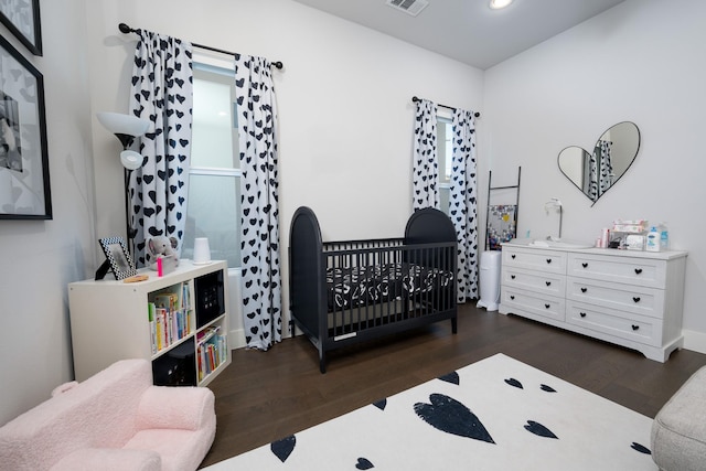 bedroom with dark wood-type flooring and a crib