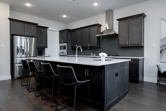 kitchen with an island with sink, wall chimney range hood, stainless steel appliances, and a kitchen breakfast bar