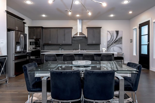 kitchen featuring a kitchen breakfast bar, appliances with stainless steel finishes, a spacious island, and wall chimney range hood