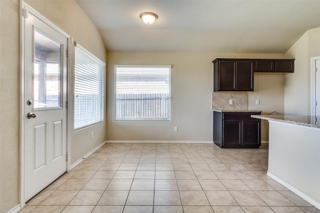 kitchen featuring light tile patterned floors, light stone countertops, dark brown cabinetry, and tasteful backsplash