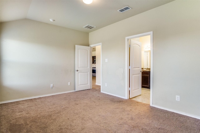 unfurnished bedroom featuring vaulted ceiling, light colored carpet, and ensuite bath