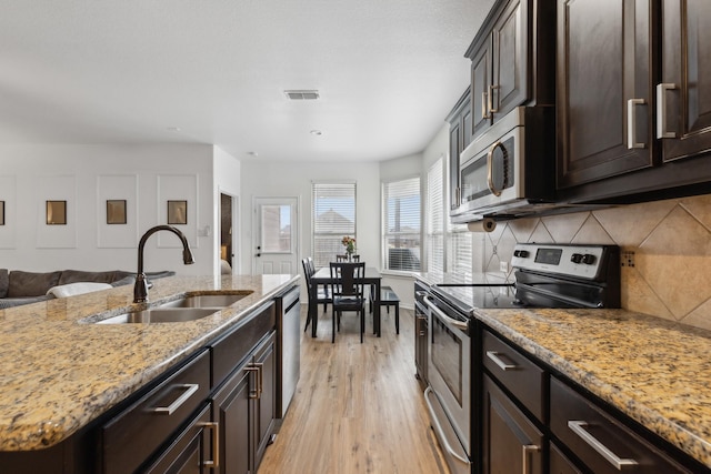 kitchen with sink, light stone counters, light hardwood / wood-style flooring, appliances with stainless steel finishes, and decorative backsplash