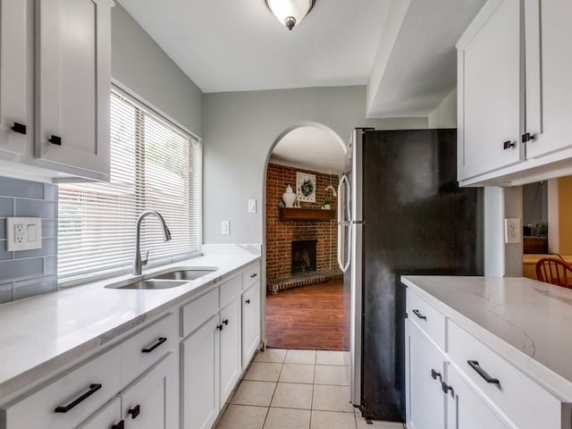 kitchen featuring white cabinetry, sink, stainless steel refrigerator, a brick fireplace, and light tile patterned floors