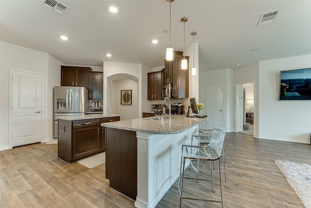 kitchen with pendant lighting, kitchen peninsula, appliances with stainless steel finishes, light stone countertops, and dark brown cabinets