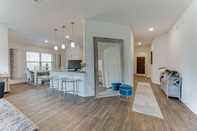 kitchen featuring kitchen peninsula, light stone counters, a breakfast bar area, and pendant lighting