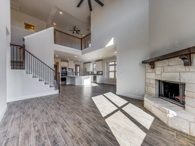 unfurnished living room featuring ceiling fan, a high ceiling, and a stone fireplace