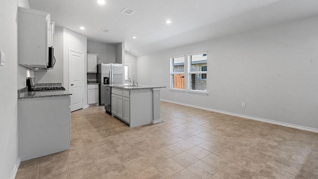 kitchen with lofted ceiling, an island with sink, sink, light stone counters, and stove